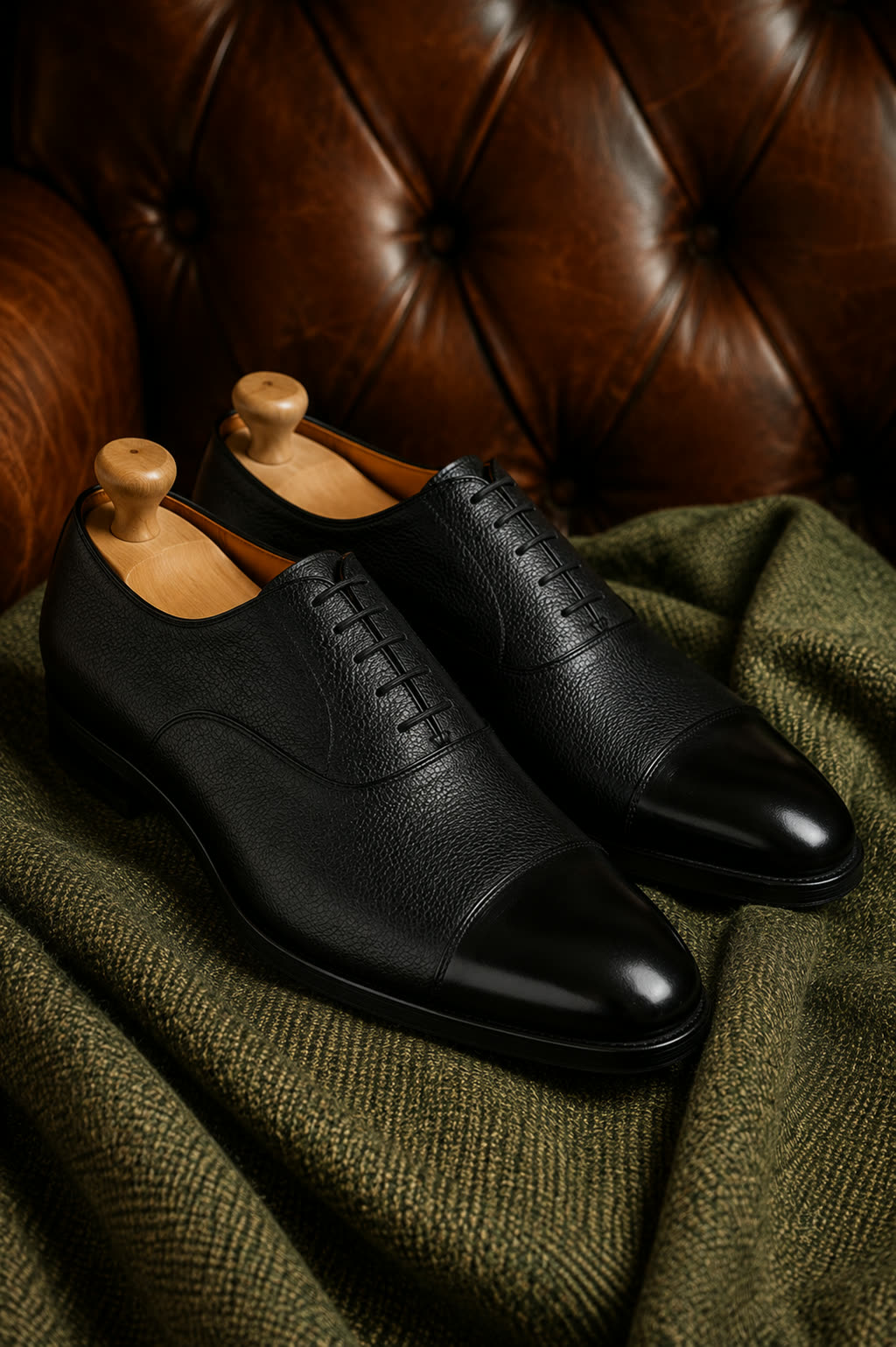 The same pair of oxfords on wooden shoe trees, against a buttoned leather chesterfield sofa