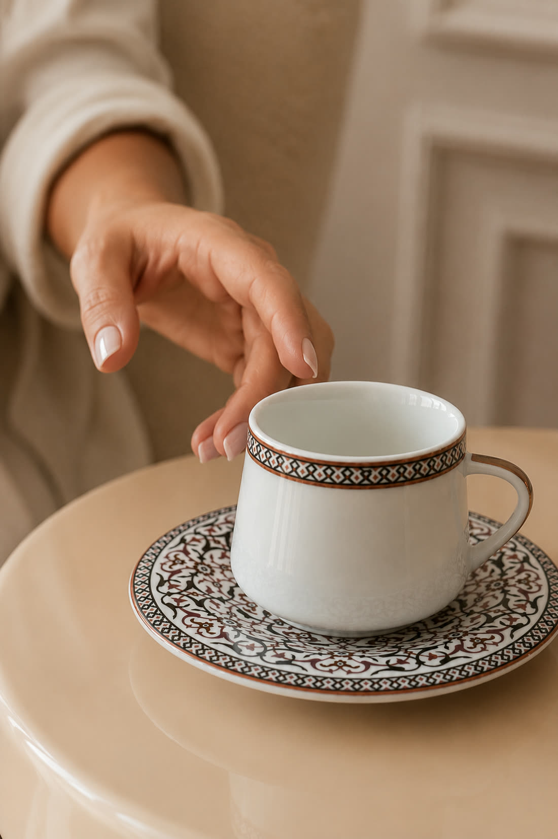 A hand reaching for the same cup, the border pattern on the cup and saucer held exactly