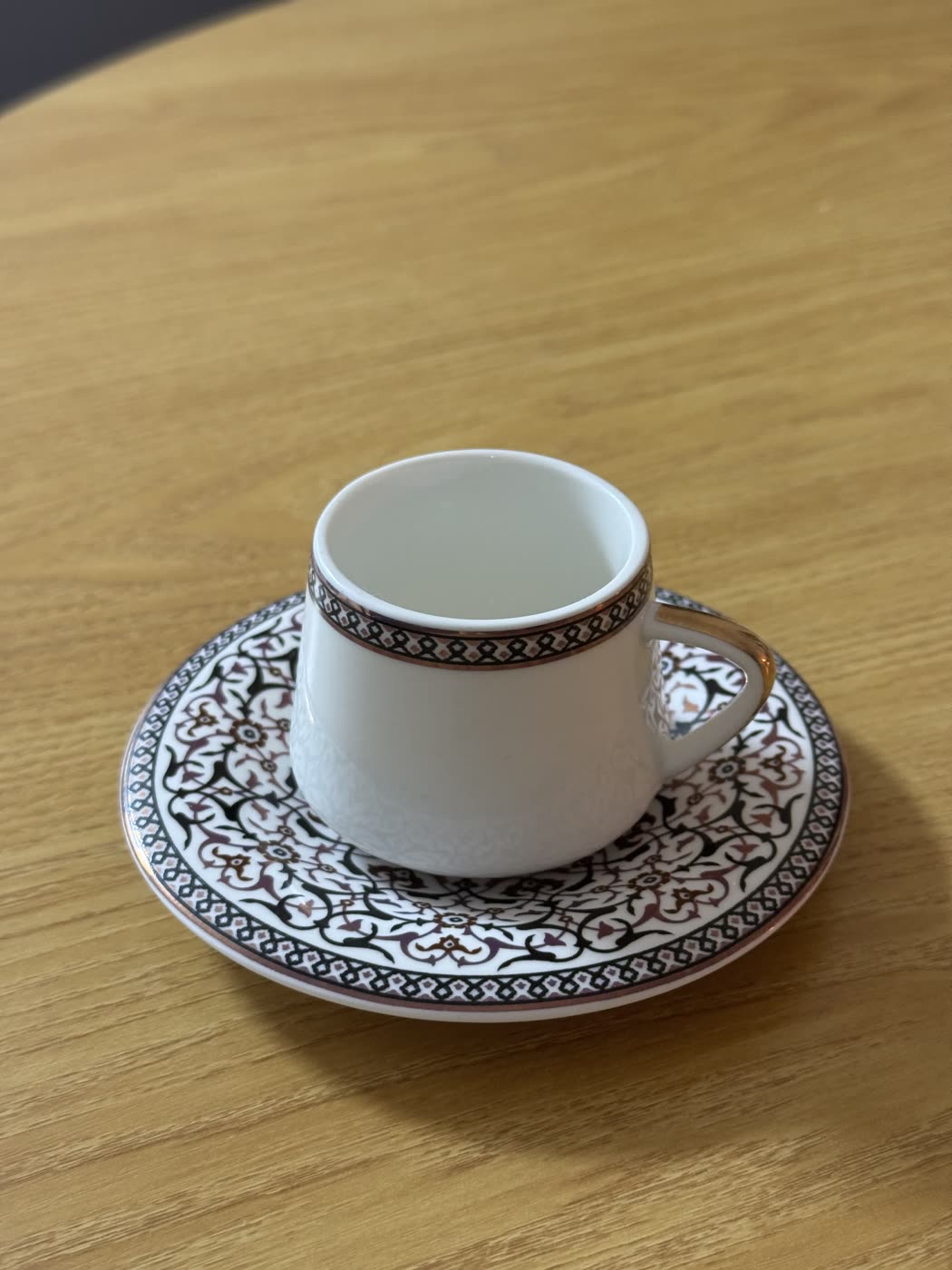 Phone photograph of a patterned coffee cup and saucer, poorly lit