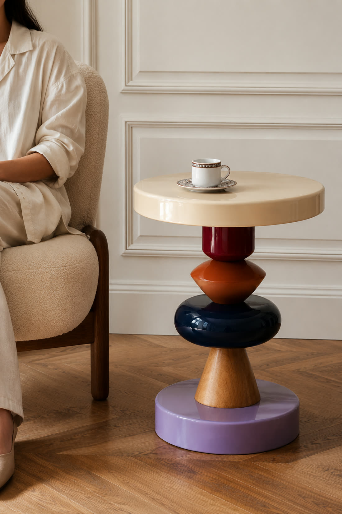 The same cup and saucer styled on a sculptural side table beside a seated woman in a boucle armchair