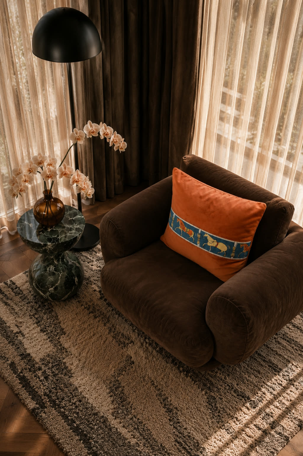 The same cushion styled on a dark velvet armchair beside a floor lamp and an orchid, warm afternoon light