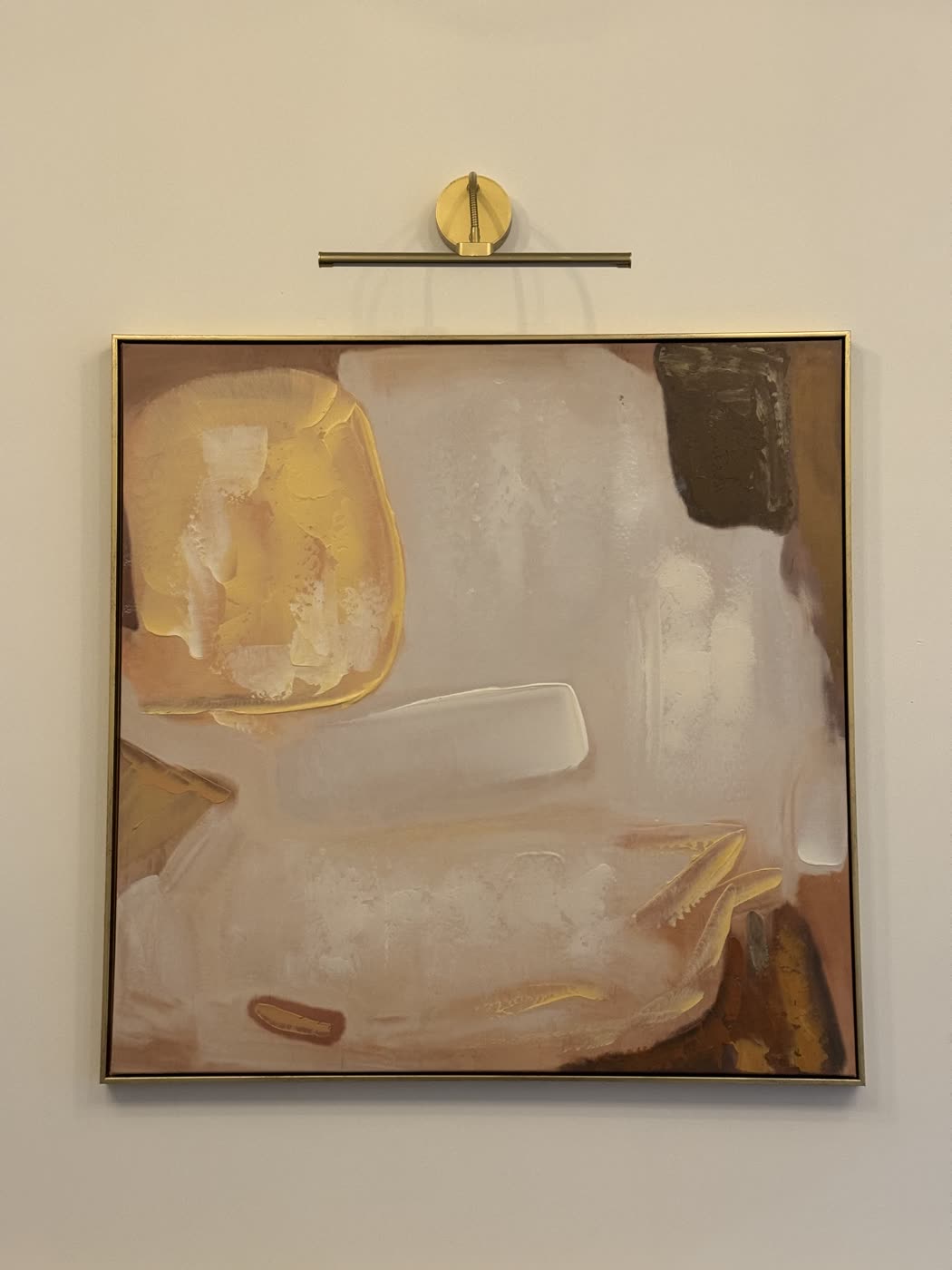 Phone photograph of a framed abstract painting propped against a wall under a picture light