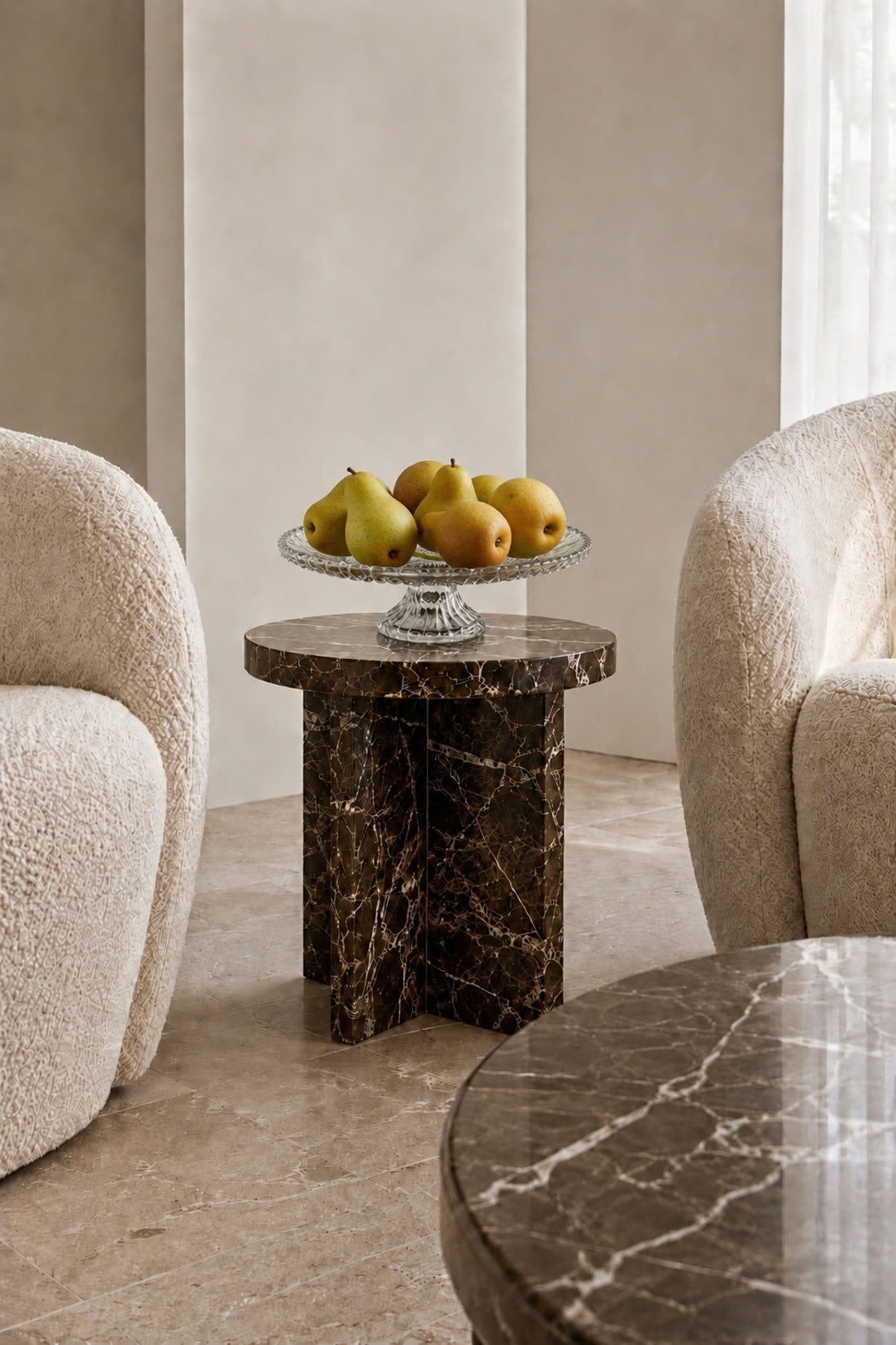 The same stand holding pears, styled on a marble side table between two boucle armchairs
