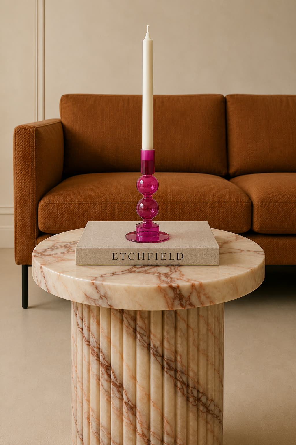 The candle holder on a fluted marble side table beside a rust velvet sofa