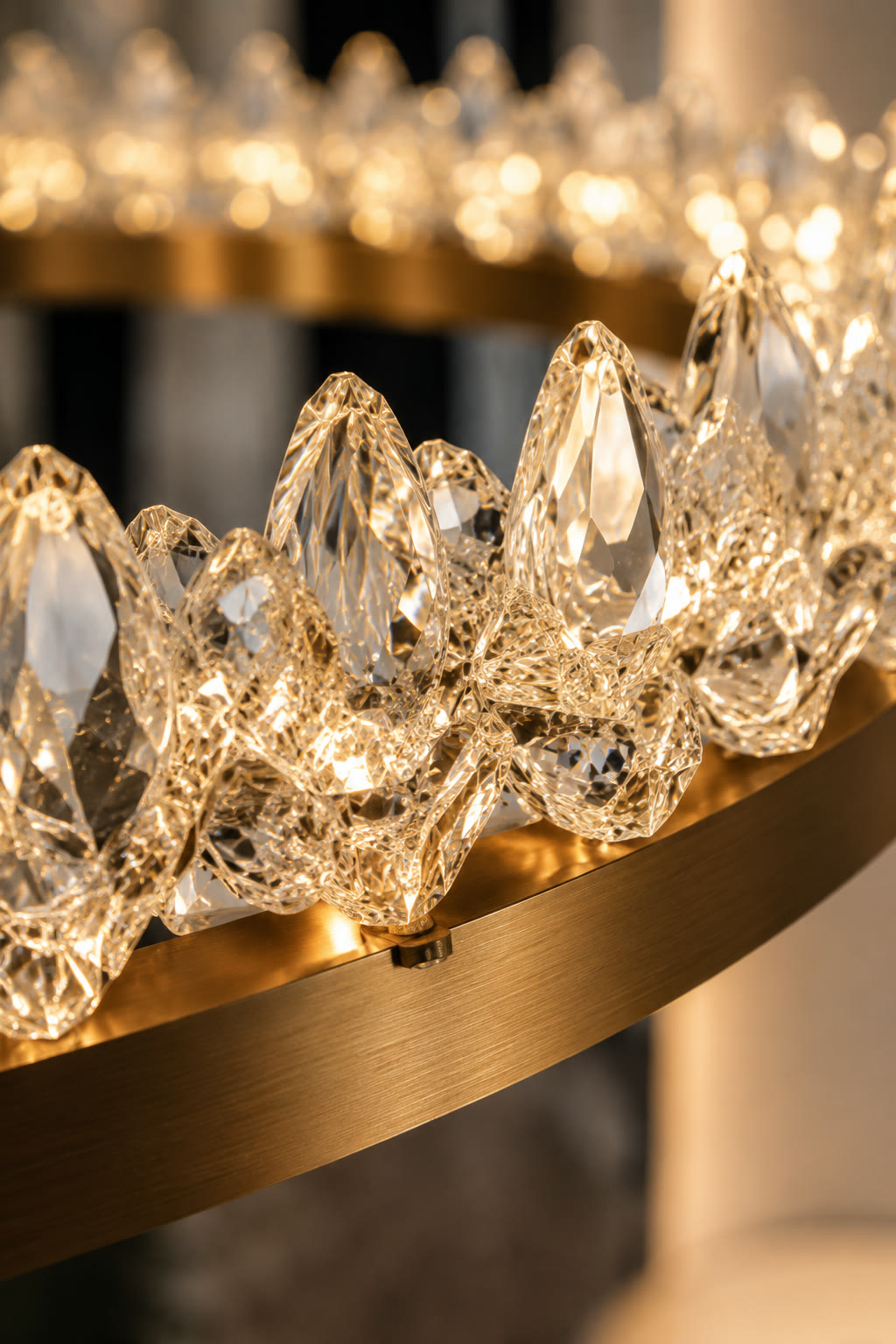 Detail of a crystal and brushed brass ring chandelier, the faceted drops lit from within