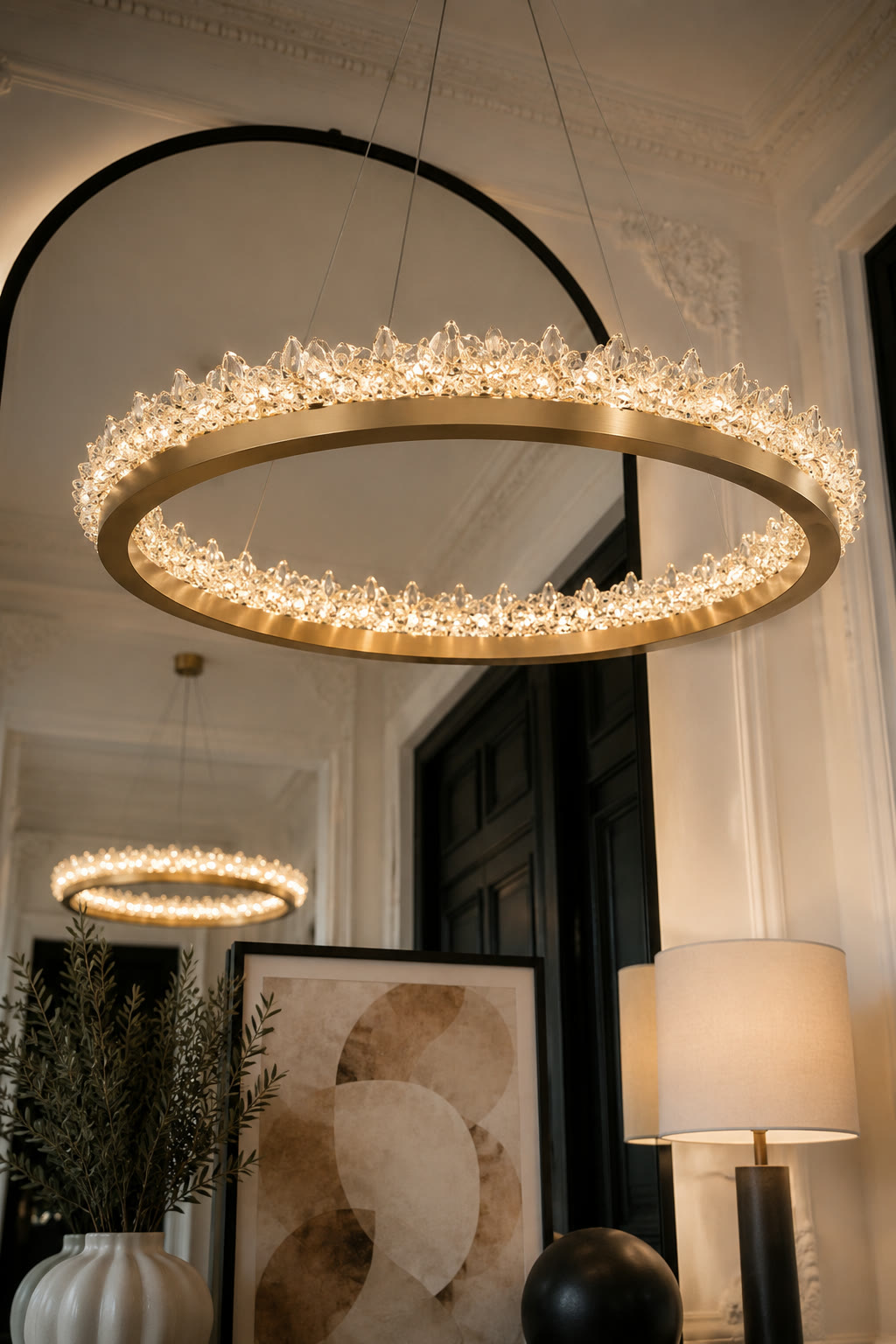 The full crystal ring chandelier hanging in a panelled hallway, an arched mirror behind it