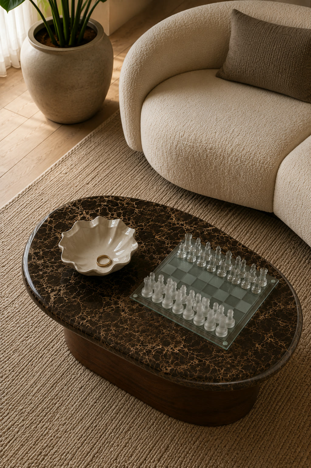 A frosted glass chess set and a scalloped ceramic ring bowl on a dark marble side table between two boucle armchairs