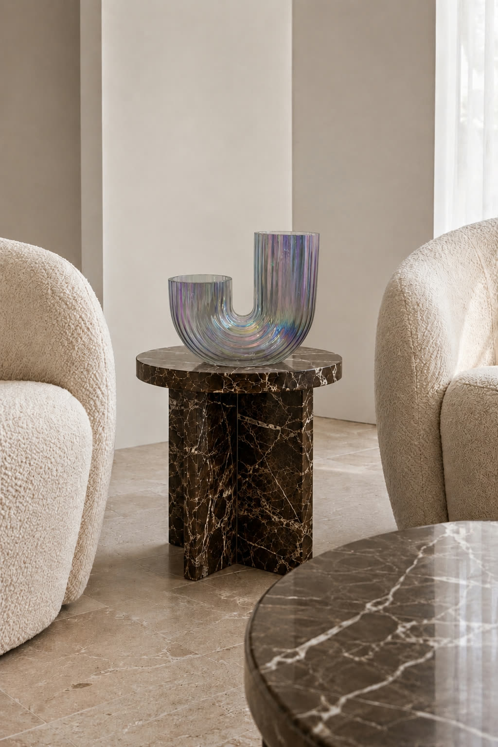The glass sculpture on a dark marble side table between two boucle armchairs