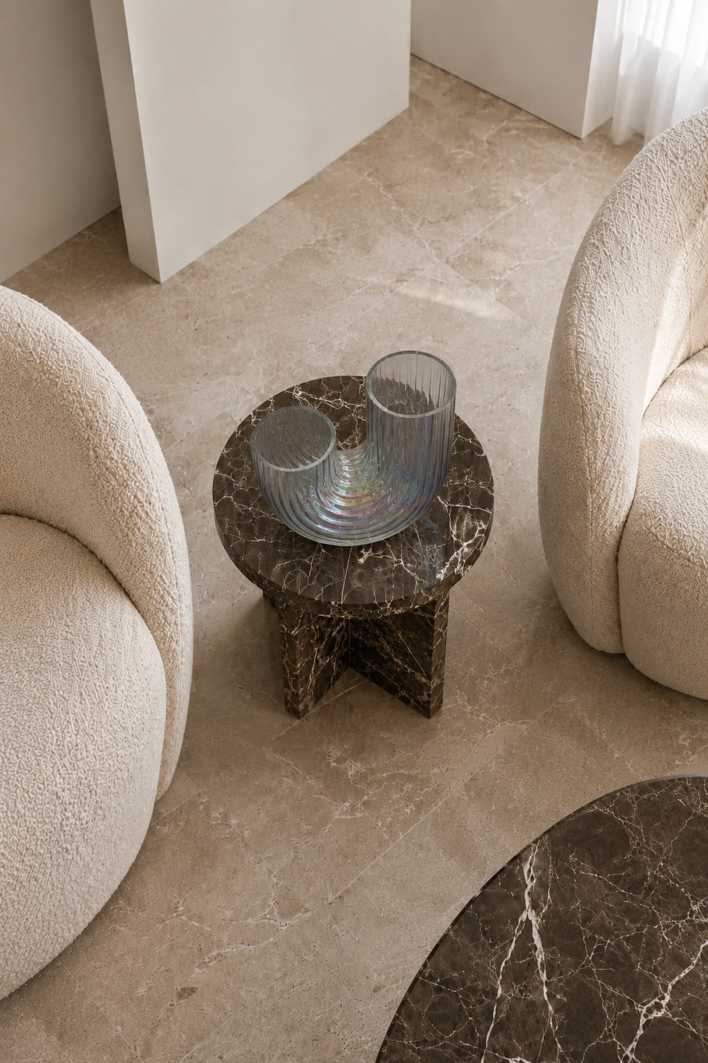 The glass sculpture seen from above, on a small marble table between two boucle armchairs