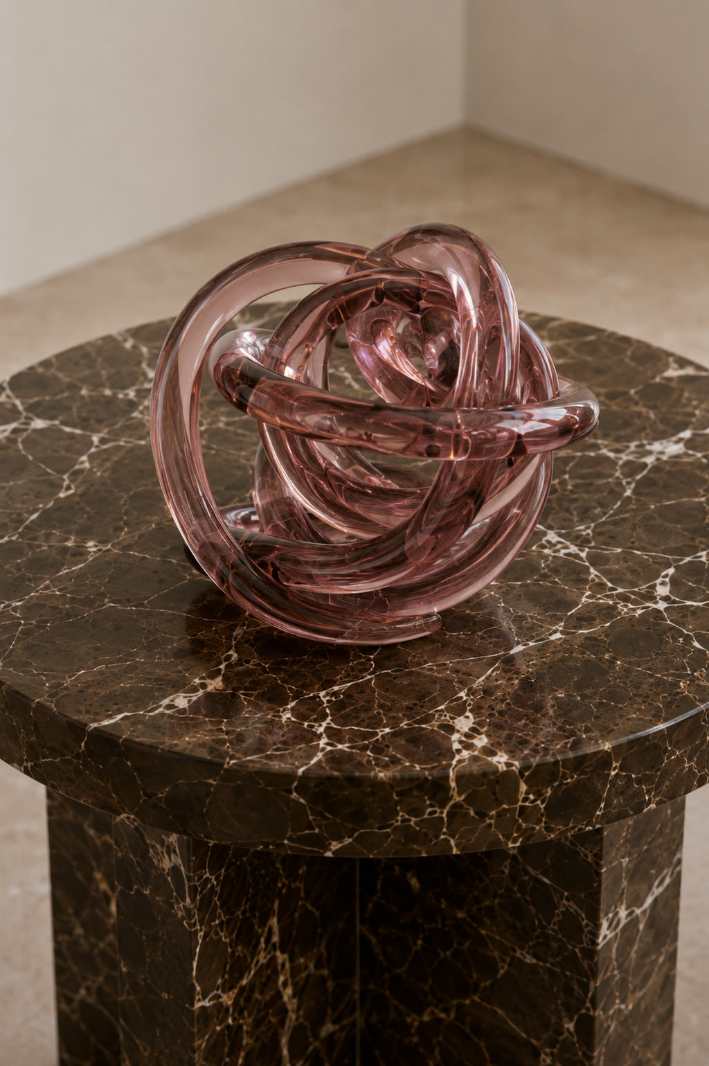 A rose glass knot sculpture on a dark marble side table