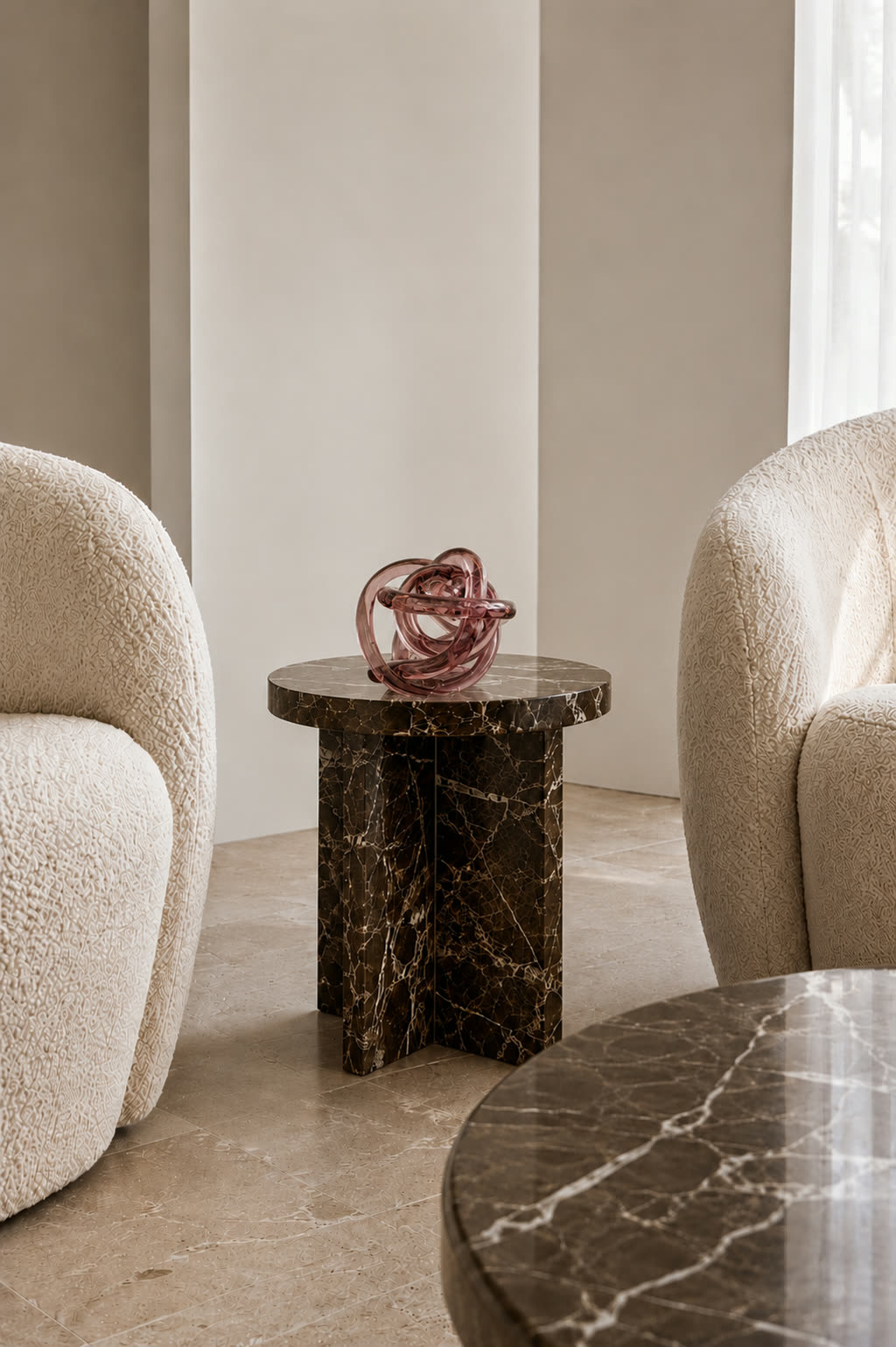 The glass knot sculpture on a low side table in a room with pale boucle armchairs
